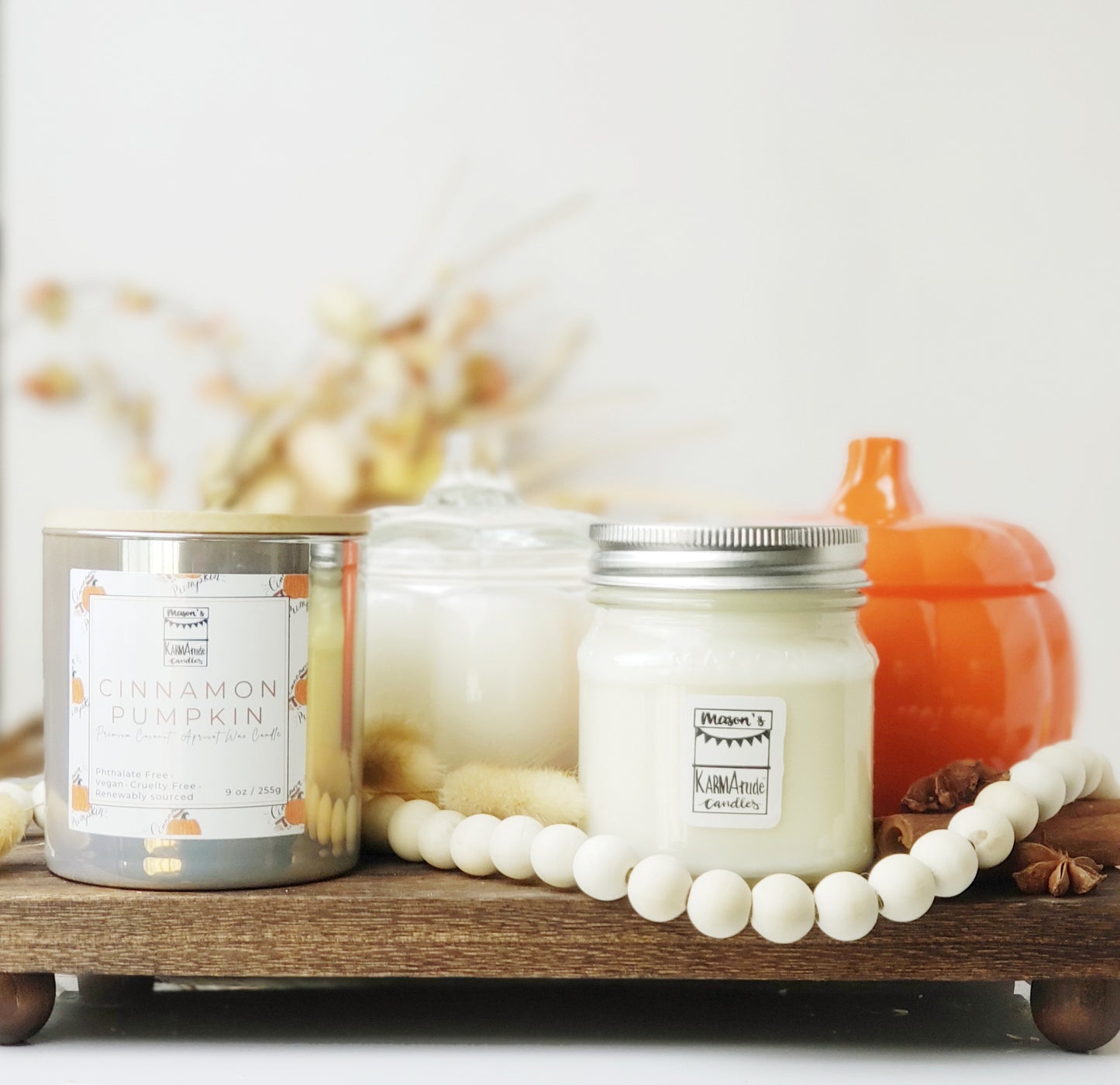 Assorted fall candles with clear glass pumpkin, orange glass pumpkin, taupe iridescent cinnamon pumpkin candle with lid, and mason jar candle surrounded by fall decor. 