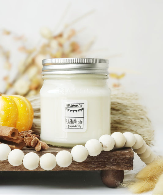 Clear Glass pumpkin candle with lid surrounded by wood beads, cinnamon, and fluffy decor on a wood tray.