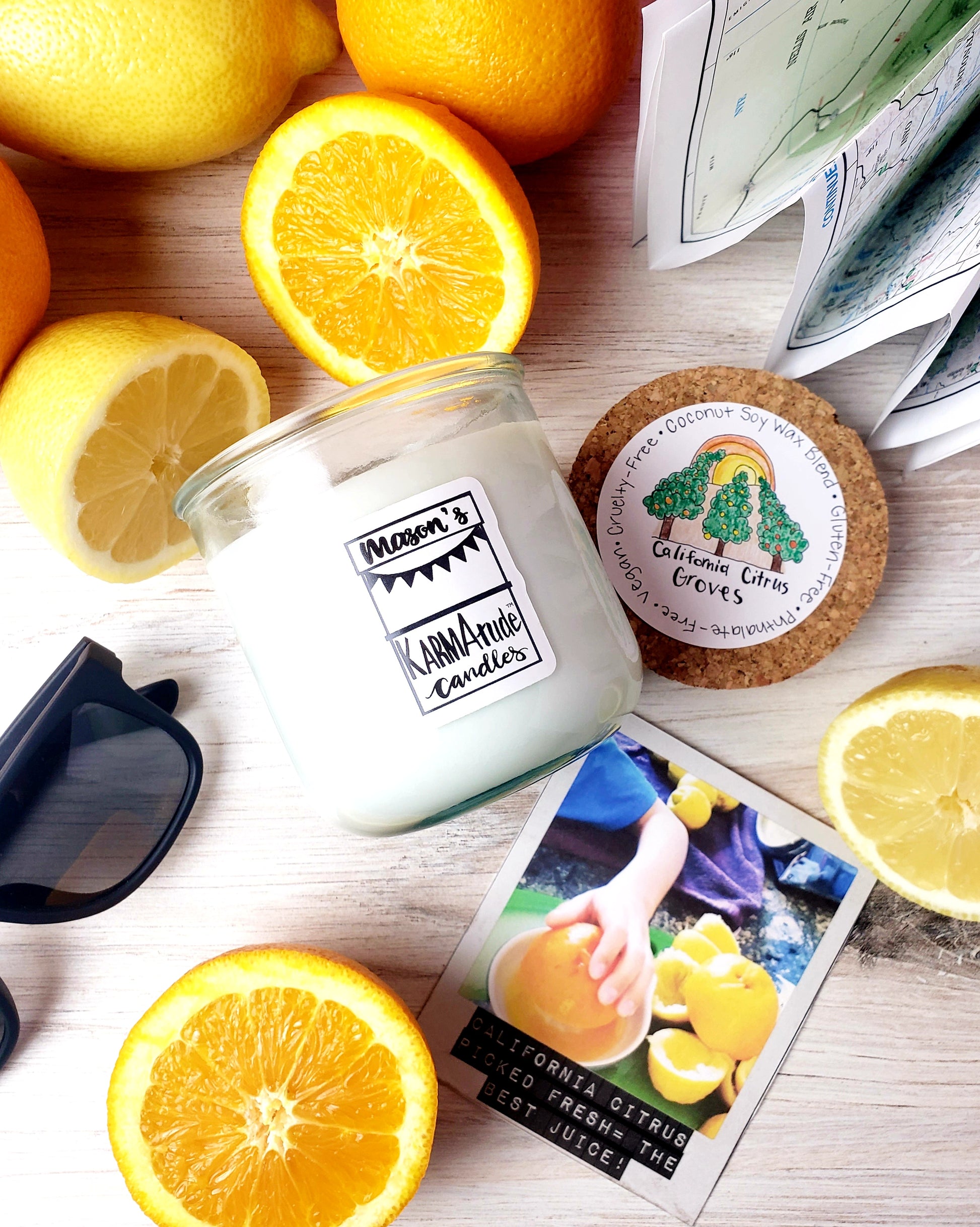 Photo of California Citrus Groves Karmatude candle in clear glass jar with cork lid surrounded by citrus, map and sunglasses.