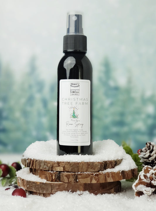 Christmas Tree Farm room spray in black bottle with lid on stacked wood coasters in the snow with berries and snow cones.