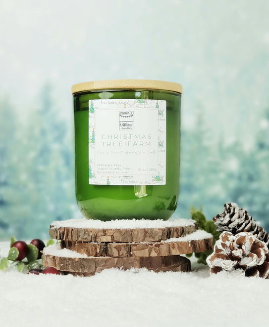 Picture of green glass candle with wood lid in Christmas Tree Farm scent on wood and snow platform.