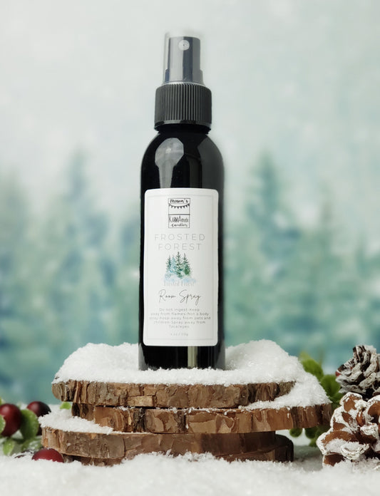 Frosted Forest room spray in black bottle with lid on stacked wood coasters in the snow with berries and snow cones.