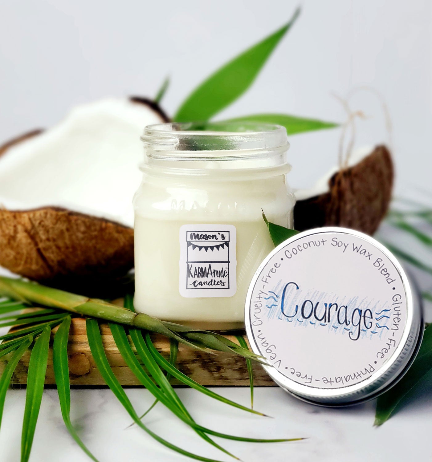 Karmatude Candles Courage candle in clear Mason jar with lid surrounded by palm fronds and coconut.