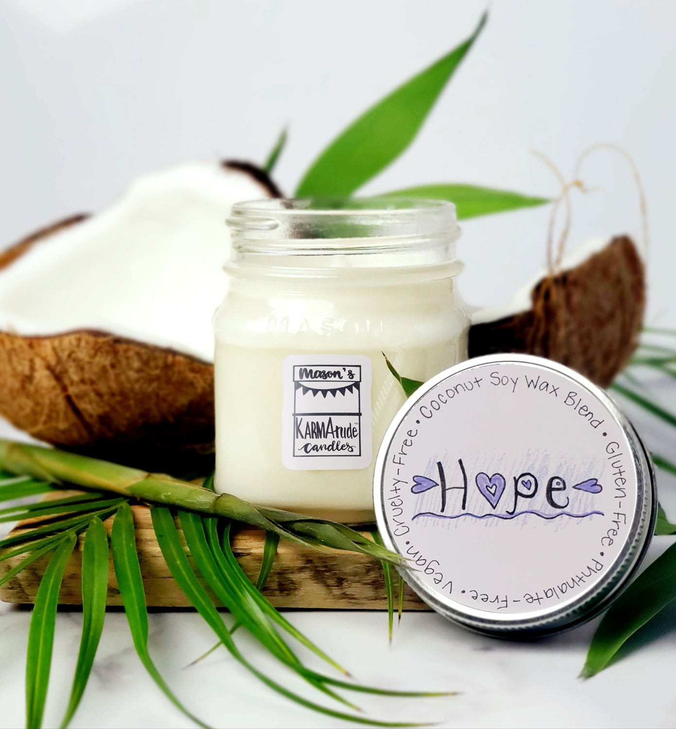 Karmatude Candles Hope candle in clear Mason jar with lid surrounded by palm fronds and coconut.