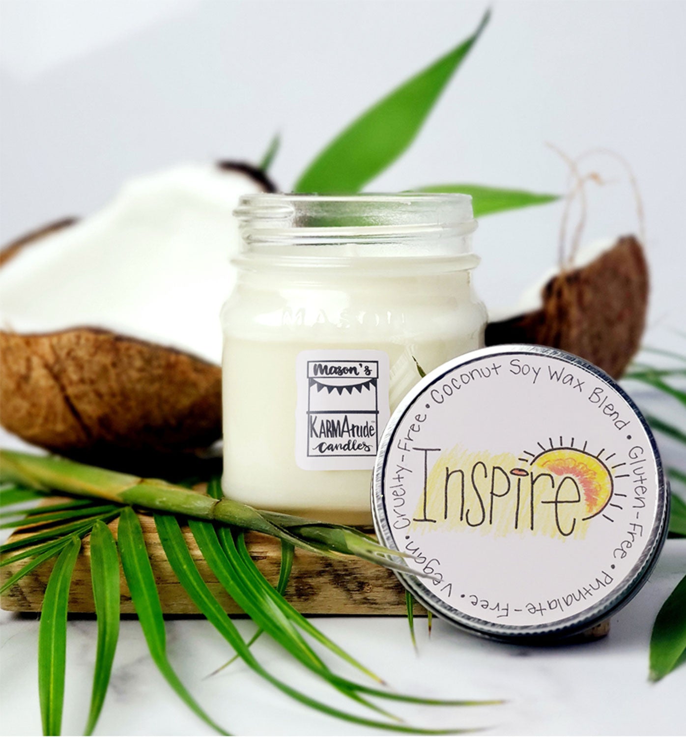 Karmatude Candles Inspire candle in clear Mason jar with lid surrounded by palm fronds and coconut.