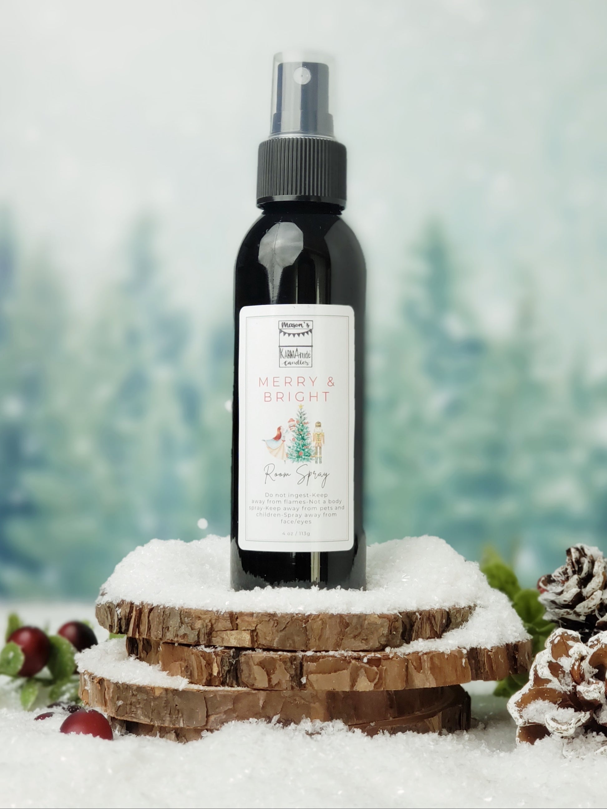 Merry and Bright room spray in black bottle with lid on stacked wood coasters in the snow with berries and snow cones.