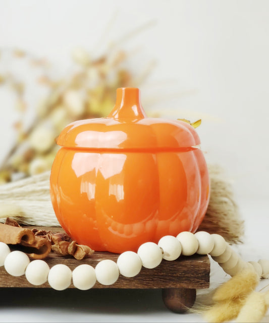 Orange Glass pumpkin candle with lid surrounded by wood beads, cinnamon, and fluffy decor on a wood tray.