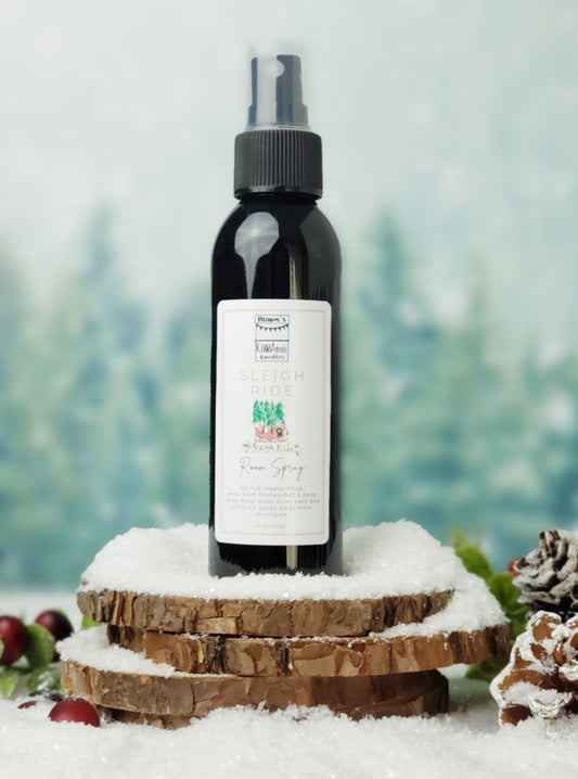 Sleigh Ride room spray in black bottle with lid on stacked wood coasters in the snow with berries and snow cones.