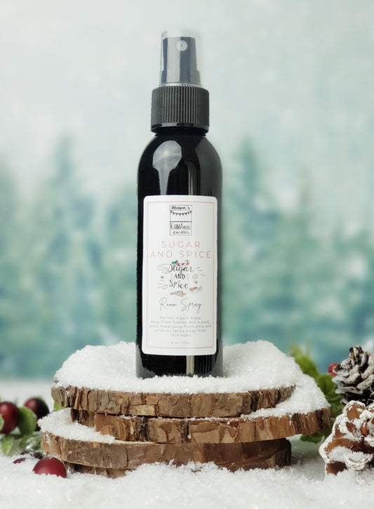 Sugar and Spice room spray in black bottle with lid on stacked wood coasters in the snow with berries and snow cones.