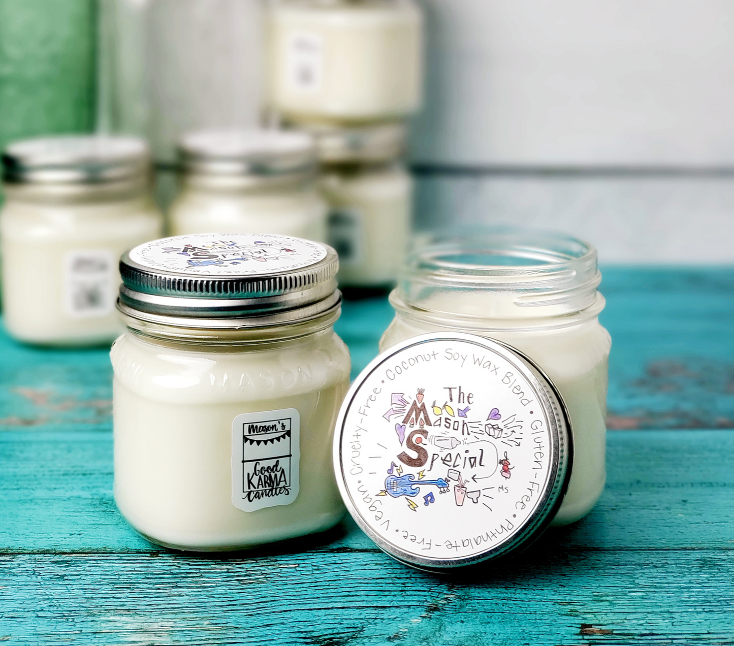 The Mason Special candle with name written on lid of Mason Jar clear glass candle  surrounded by other candles on blue wood surface.